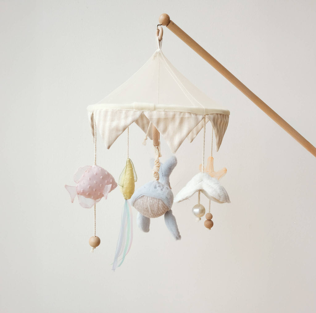 The Nautical Dreams Mobile features a wooden arm and scalloped fabric canopy, with soft plush fish, leaf, bird, and whale toys—perfect as soothing neutral nursery decor.