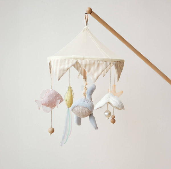 The Nautical Dreams Mobile features a wooden arm and scalloped fabric canopy, with soft plush fish, leaf, bird, and whale toys—perfect as soothing neutral nursery decor.