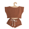 Mrs. Ertha Doll Clothes - 13″-14″ - Rusted Comfy Set features a two-piece brown toddler outfit with a short-sleeve crop top and drawstring shorts, displayed on a hook-shaped cardboard hanger—perfectly sized for Minikane dolls or as charming handmade doll clothes.