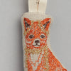 A close-up of the Fox Tree Trimmer Ornament reveals intricate stitching in shades of orange, brown, and gold. The fox is elegantly positioned on a beige background, featuring a loop at the top and evoking holiday memories against a simple gray backdrop. This ornament makes an ideal Christmas gift for those who appreciate nature.