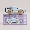 A wooden toy car modeled after a vintage sports car rests atop a box labeled “No. 23 GT130 Dexter | Pre order Aug 2026.” The packaging emphasizes its sustainable wood construction, child-safe paints, and British craftsmanship, making this modern toy ideal for imaginative play.