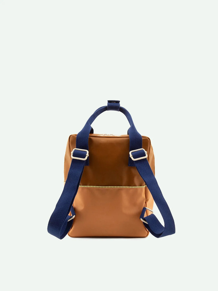 A Sticky Lemon Backpack Small in Treehouse Brown with a sleek design featuring a front YKK zipper and adjustable blue straps, displayed against a plain white background.