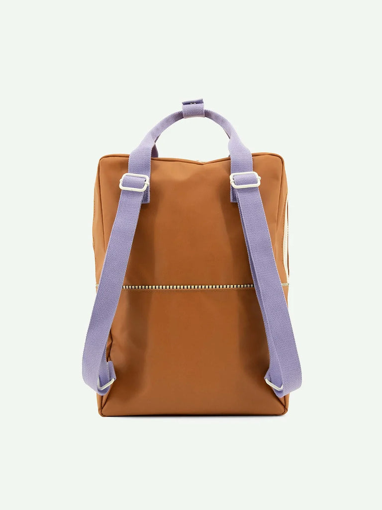 A Sticky Lemon Backpack | Uni | Buddy Brown with a front YKK zipper pocket and contrasting light purple adjustable straps, displayed against a plain white background.