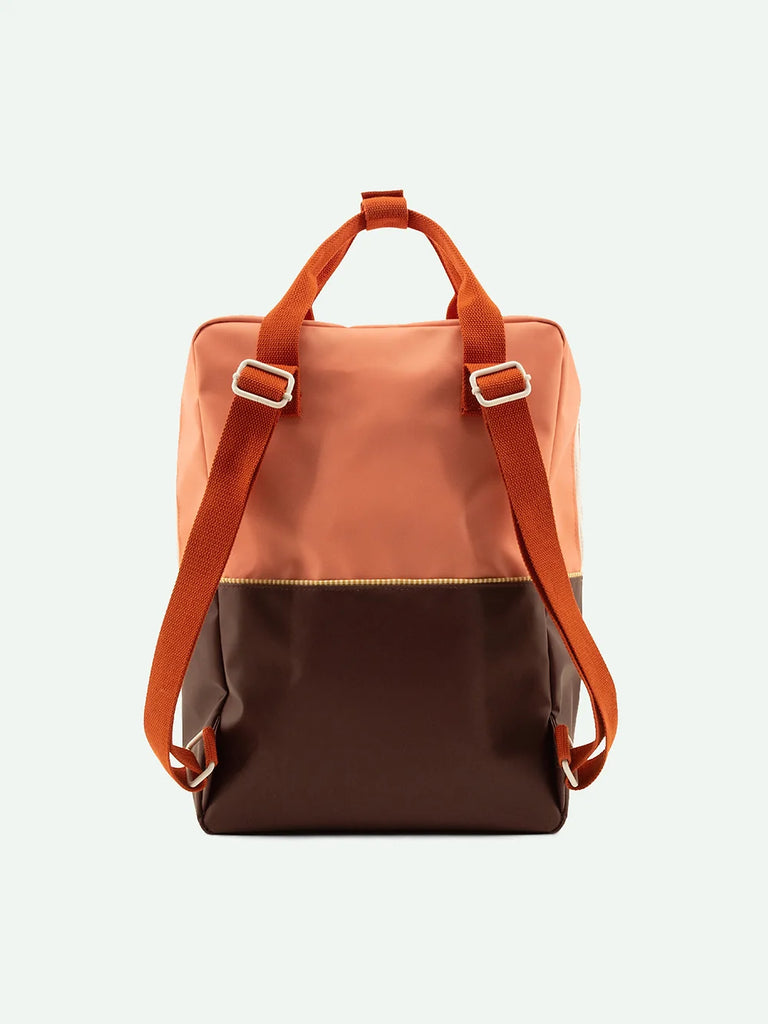 A modern Sticky Lemon Backpack Large featuring a Moonrise Pink upper and a dark brown lower section, with sturdy orange straps made from waterproof nylon, displayed against a plain white background.