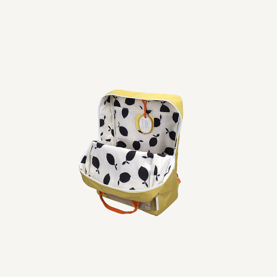 A large green Sticky Lemon "Envelope - Bookworm Green" backpack, designed for kids, with orange handles and a round yellow luggage tag hanging inside. Unzipped to reveal its white interior lining decorated with a black leaf pattern, this waterproof bag is made from recycled PET bottles.