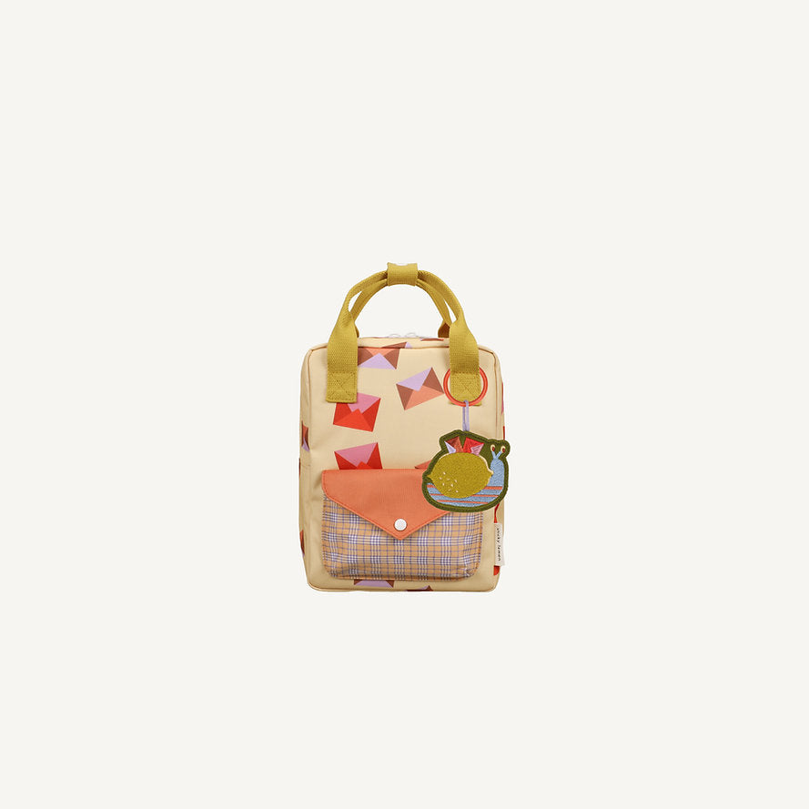The Sticky Lemon Backpack Small - Special Edition - Snail Mail is a beige kids backpack with colorful geometric patterns, yellow handles, an orange plaid-detailed front pocket, a green snail keychain, and a waterproof lining from recycled PET bottles.