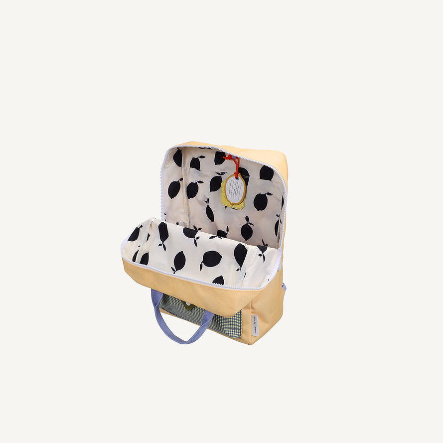 The Sticky Lemon Backpack Large - Envelope - Twiggy Beige is open, showing a white interior with black fruit pattern. Made from recycled PET bottles, it features blue handles and a yellow round keychain on the zipper pull inside.
