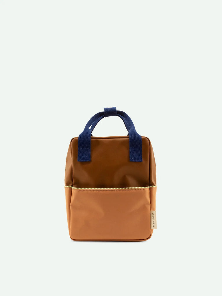 A Sticky Lemon Backpack Small in Meet Me In The Meadows color blocking, with a Treehouse Brown handle and a YKK zippered front pocket, set against a plain light background.