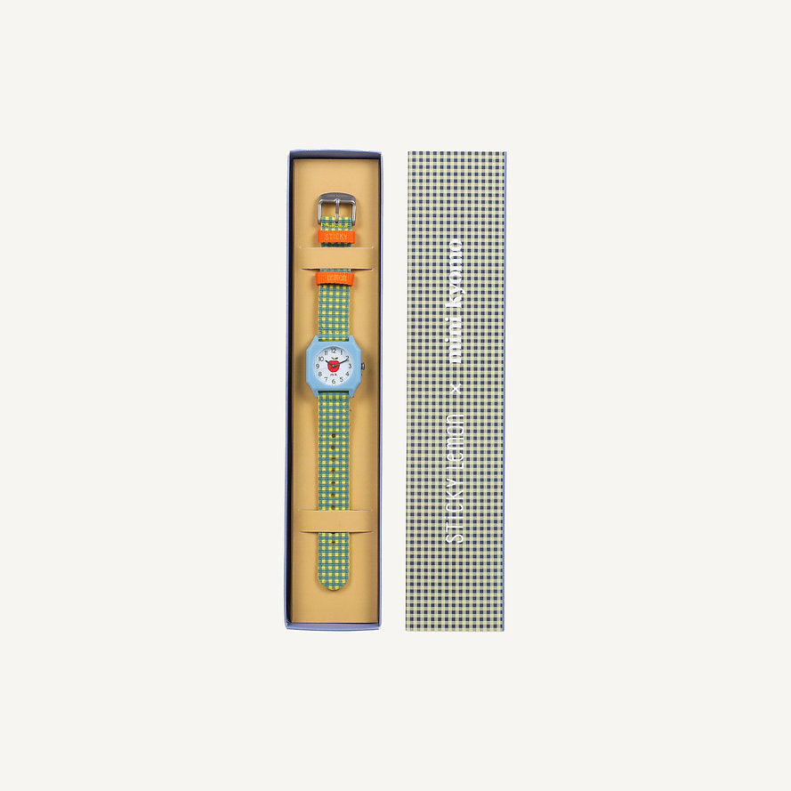 The Sticky Lemon x Mini Kyomo Watch - Apple features a green and white checkered design with a red heart on the face. It comes in a matching checkered box with Japanese text on the lid and includes a small accessory inside.