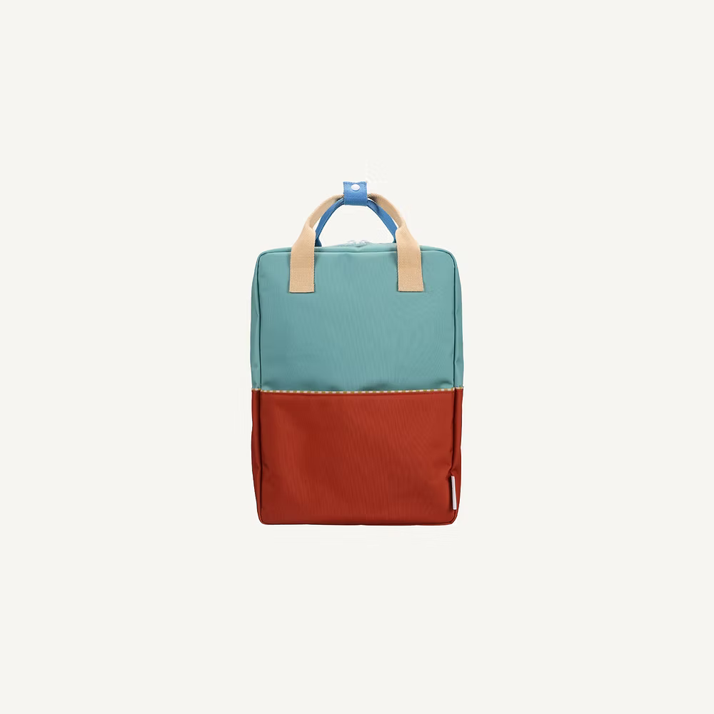 The Sticky Lemon Backpack Large | Color Blocking in Aquatic Green + Shipwreck Rust is a kids backpack with a teal top, red bottom, beige handles, blue loop, waterproof lining, and recycled PET material, shown on a plain white background.