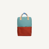 The Sticky Lemon Backpack Large | Color Blocking in Aquatic Green + Shipwreck Rust is a kids backpack with a teal top, red bottom, beige handles, blue loop, waterproof lining, and recycled PET material, shown on a plain white background.