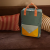 The Sticky Lemon Backpack Large | Envelope | Diving Suit, made from recycled PET with a waterproof lining, features blue with orange striped handles and yellow/light blue pocket. It sits on a brown sofa with red/white and beige/white striped cushions.