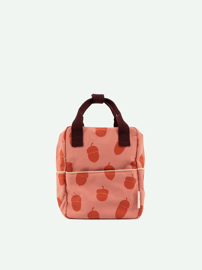 A small, peach-colored Sticky Lemon Backpack Small from the Envelope Collection, featuring a pattern of red apples, brown handles, a front zipper, displayed against a plain light background.