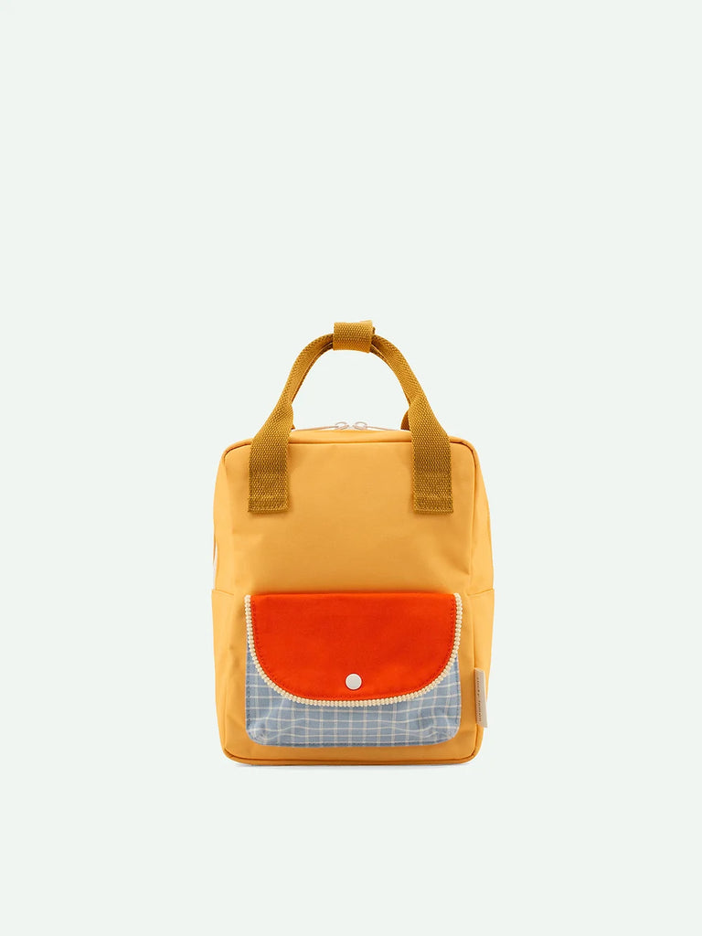 A Sticky Lemon Backpack Small in Farmhouse, with an Envelope front flap pocket in Pear Jam and a blue plaid design below it, made from waterproof nylon, against a plain light background.