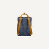 The Sticky Lemon Backpack Large | Special Edition Eyes in Boxing Blue is a square-shaped, navy blue backpack adorned with a pattern of small, white crescent moons. Made from recycled PET bottles, it features mustard yellow shoulder straps and a top handle. Enhanced with waterproof lining, it sits against a plain off-white background.