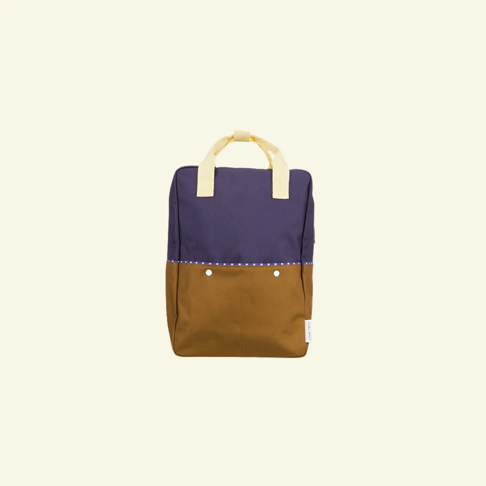A Sticky Lemon Backpack Large in the "Skate Ramp + Golden Cup" color blocking. It features a purple top half and a brown bottom half, yellow handles, small white buttons in the center of the front, adjustable shoulder straps, and a simple, clean design.