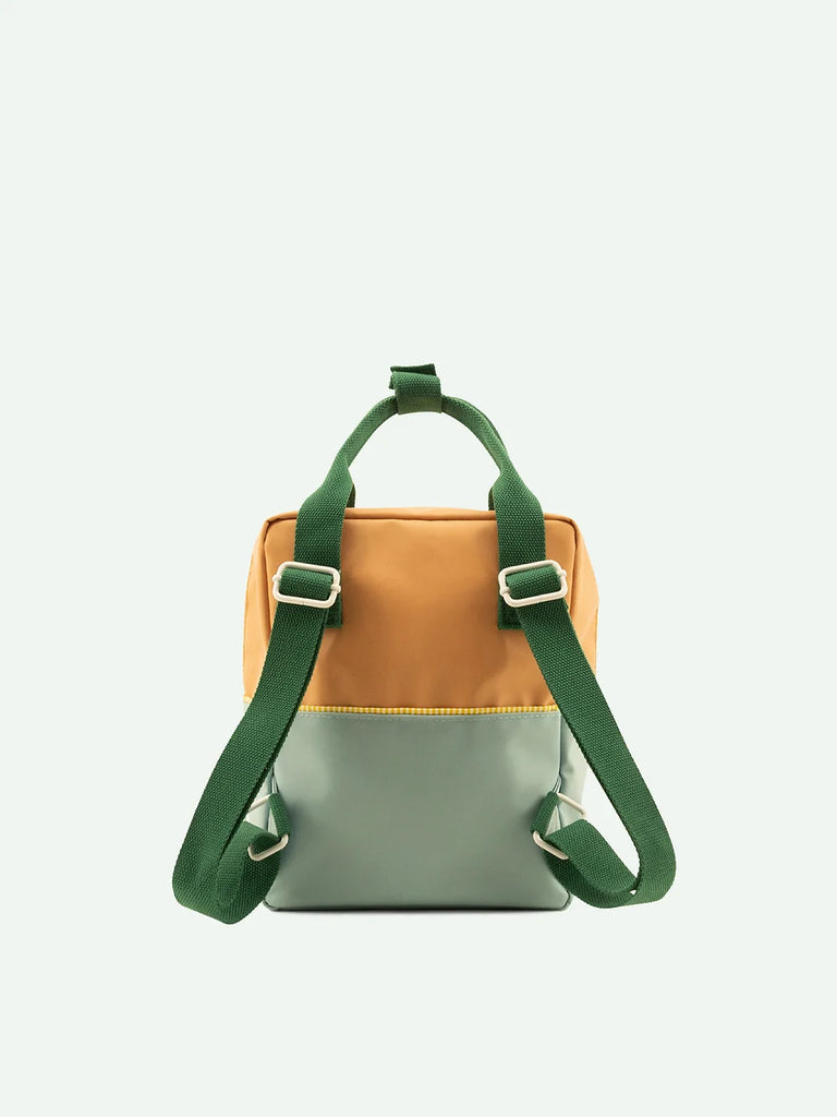 A Sticky Lemon Backpack Small with a color-block design featuring pastel yellow, green, and light gray segments, complemented by a broad green adjustable shoulder strap with a YKK zipper. The bag is displayed against.