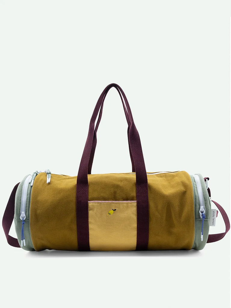 A khaki green cylindrical duffel bag with dark purple adjustable shoulder handles and side straps. The bag features external pockets and a small logo near the center.