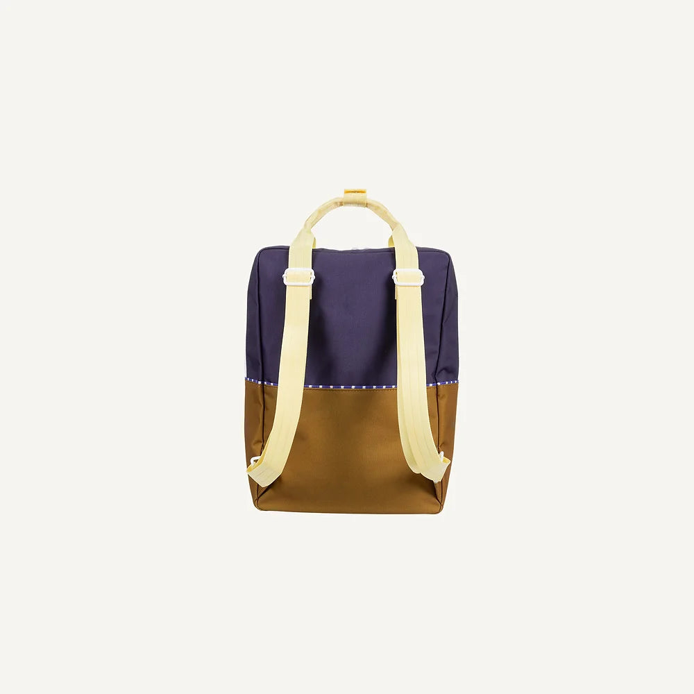 The Sticky Lemon Backpack Large | Color Blocking | Skate Ramp + Golden Cup is a two-toned backpack crafted from recycled PET, featuring a dark blue upper half and a brown lower half. It includes cream-colored adjustable shoulder straps and a top handle for easy carrying, along with a waterproof lining. The bag is showcased against a plain, light background.