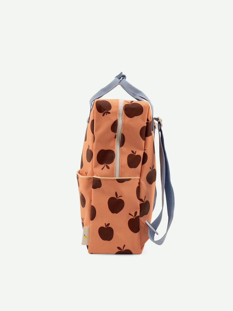 A peach-colored Sticky Lemon Backpack Large | Special Edition with a dark apple print, featuring front and side pockets, a top handle, adjustable shoulder straps, and waterproof lining, displayed against a white background.