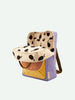 A Sticky Lemon Backpack Large with the flap open, revealing a cheerful dotted interior. The backpack combines a beige, black, mustard, and purple palette and is made from waterproof nylon.