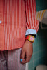 A person in pink striped pajamas and a Sticky Lemon x Mini Kyomo Watch - Flower with a checkered face stands in a tiled bathroom. Their fingernails are painted light blue.
