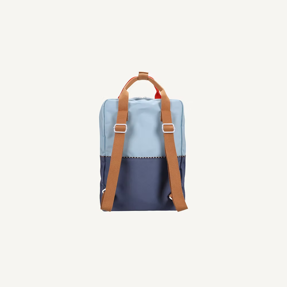 The Sticky Lemon Backpack Large | Color Blocking | Bissou Blue + Blue Whale is a two-tone kids backpack made from recycled PET bottles, with a light blue top, dark blue base, and brown adjustable straps and handle, shown from the back on a white background.
