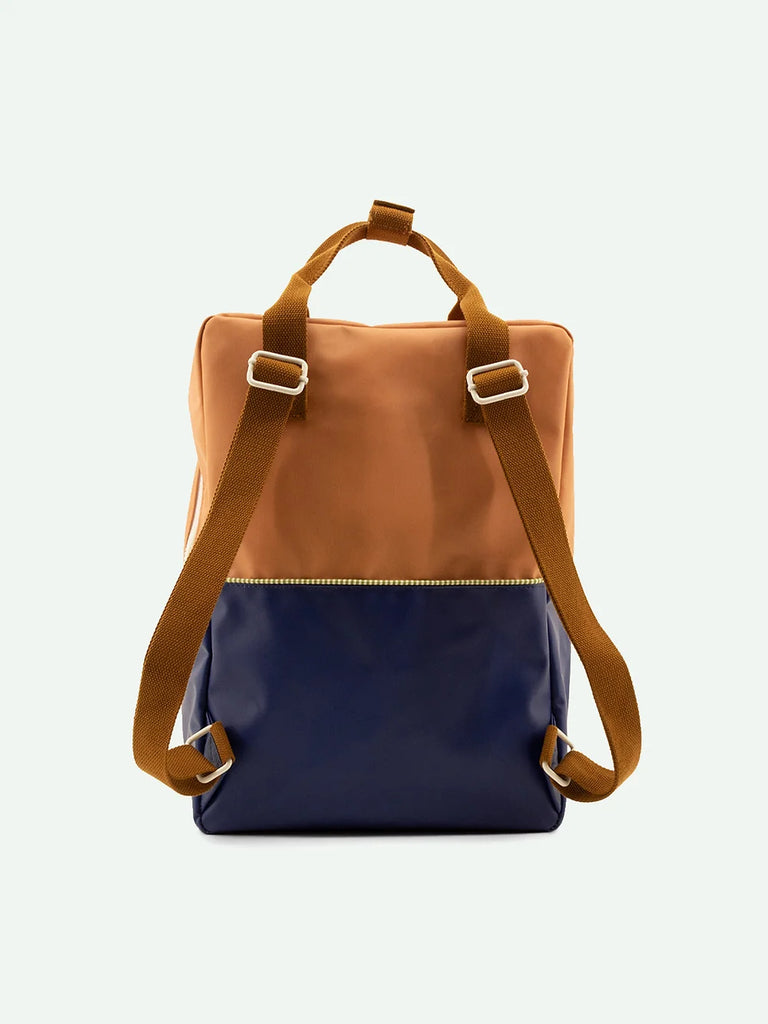 A stylish Sticky Lemon Backpack Large crafted from waterproof nylon, featuring a tan upper half and a navy blue lower half, with adjustable brown straps and a front zip pocket with a YKK zipper, isolated against a white background.