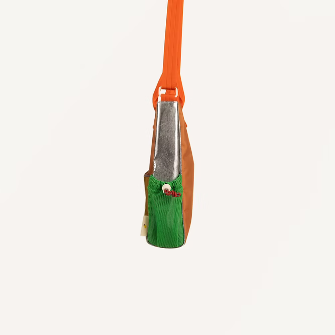 A side view of the Sticky Lemon Shoulder Bag | Leather Ball + Golden Cup shows its recycled PET design with an orange strap, metallic silver section, brown body, textured green pocket with tag, all set against a plain white background.