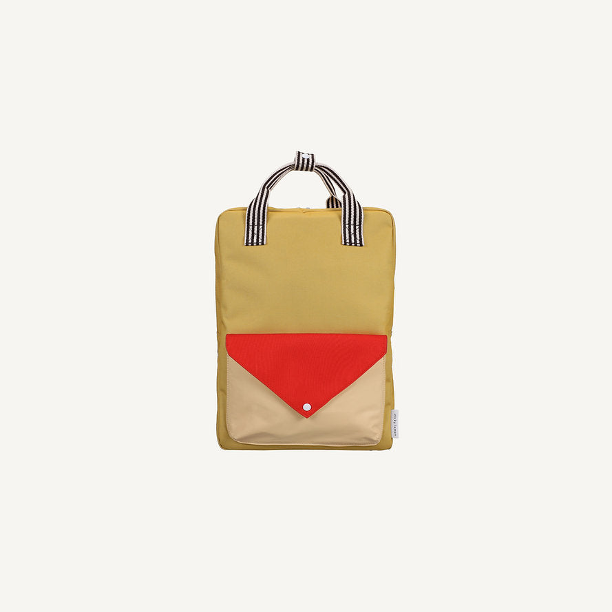 The Sticky Lemon Backpack Large - Envelope - Reed Green is a rectangular kids’ bag in yellow, featuring black-and-white striped handles and a front pocket with a red flap over a beige panel. Designed to be waterproof, it also includes adjustable shoulder straps for comfort, and is shown against a plain white background.