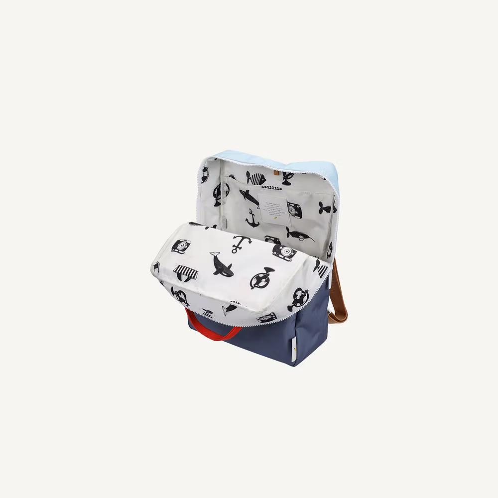 The Sticky Lemon Backpack Large | Color Blocking | Bissou Blue + Blue Whale is a blue kids backpack with a brown strap, featuring a white interior lining printed with black nautical illustrations. Made from recycled PET bottles.