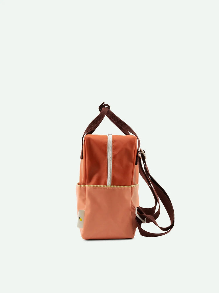 A small, Love Story Red backpack made from recycled PET bottles with a vertically centered zip pocket and contrasting dark brown straps, displayed against a plain background.
