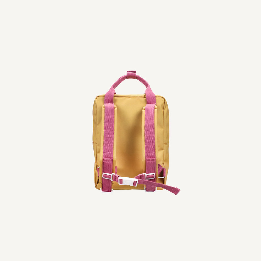 The Sticky Lemon Backpack Medium - Envelope - Apple Grub is a small yellow backpack with pink adjustable straps, a pink top handle, white buckle, and waterproof lining made from recycled PET bottles on an off-white background.