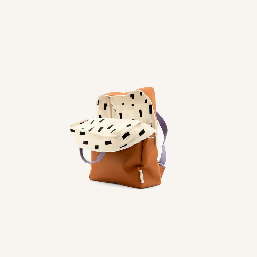 A stylish, modern Sticky Lemon Backpack | Uni | Buddy Brown featuring a beige color with black dash patterns, equipped with a fold-over top and brown leather accents, isolated on a white background and constructed from waterproof nylon.