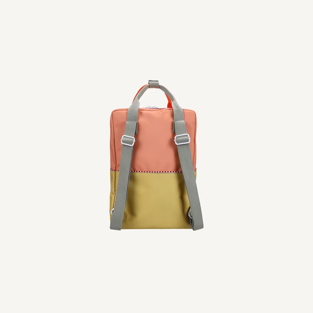 The Sticky Lemon Backpack Large | Color Blocking | Coral Pink + Reed Green features a coral pink top, reed green bottom, gray adjustable straps, and top handle. Made from recycled PET with a waterproof lining, shown on a plain light background.
