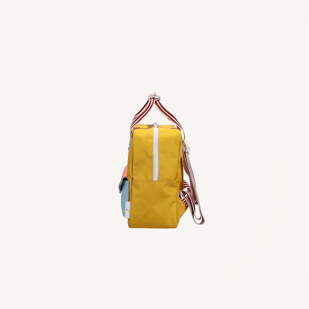 Side view of the Sticky Lemon Backpack Small from the Envelope Collection in Submarine Yellow, featuring a yellow main compartment, white zipper, red and white striped handles, blue pocket, adjustable straps; shown on white background.