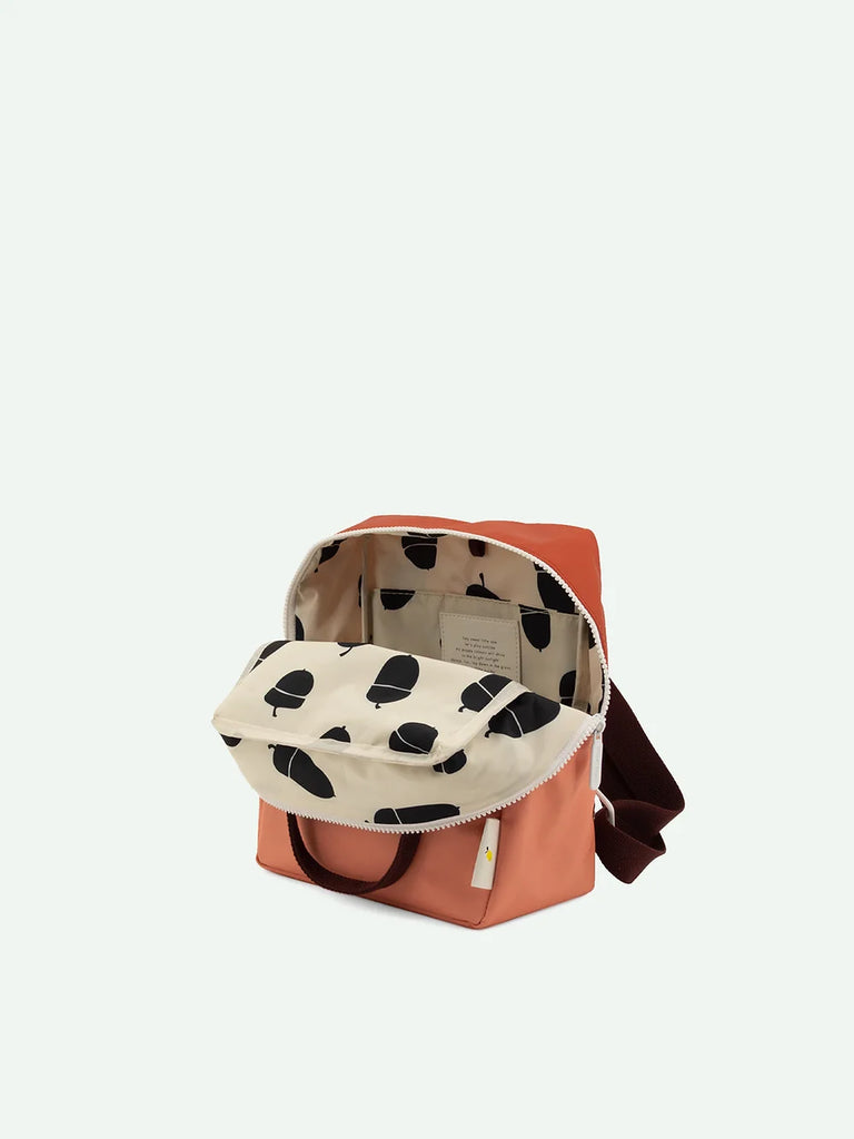 A small, open Sticky Lemon backpack in Love Story Red with a cream flap featuring a black abstract pattern and a YKK zipper. The bag's interior is visible, displaying a light beige lining made from waterproof nylon.
