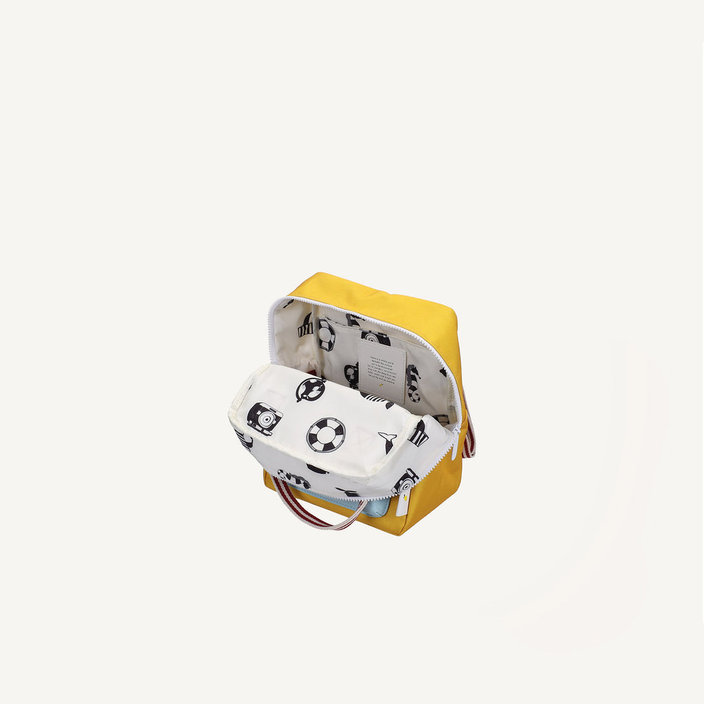The Sticky Lemon Backpack Small | Envelope Collection | Submarine Yellow features a zippered recycled PET design with a handle and opens to a white lining printed with black icons like cameras, soccer balls, and traffic cones.
