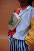 A person wearing a color-block sweatshirt, blue and white striped pants, and the Sticky Lemon Fanny Pack Small - Envelope - Tickling Grass stands against a plain brown background.