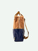 Two-tone Sticky Lemon backpack in tan and navy, standing upright against a white background, featuring external pockets and adjustable shoulder straps with a waterproof nylon construction.