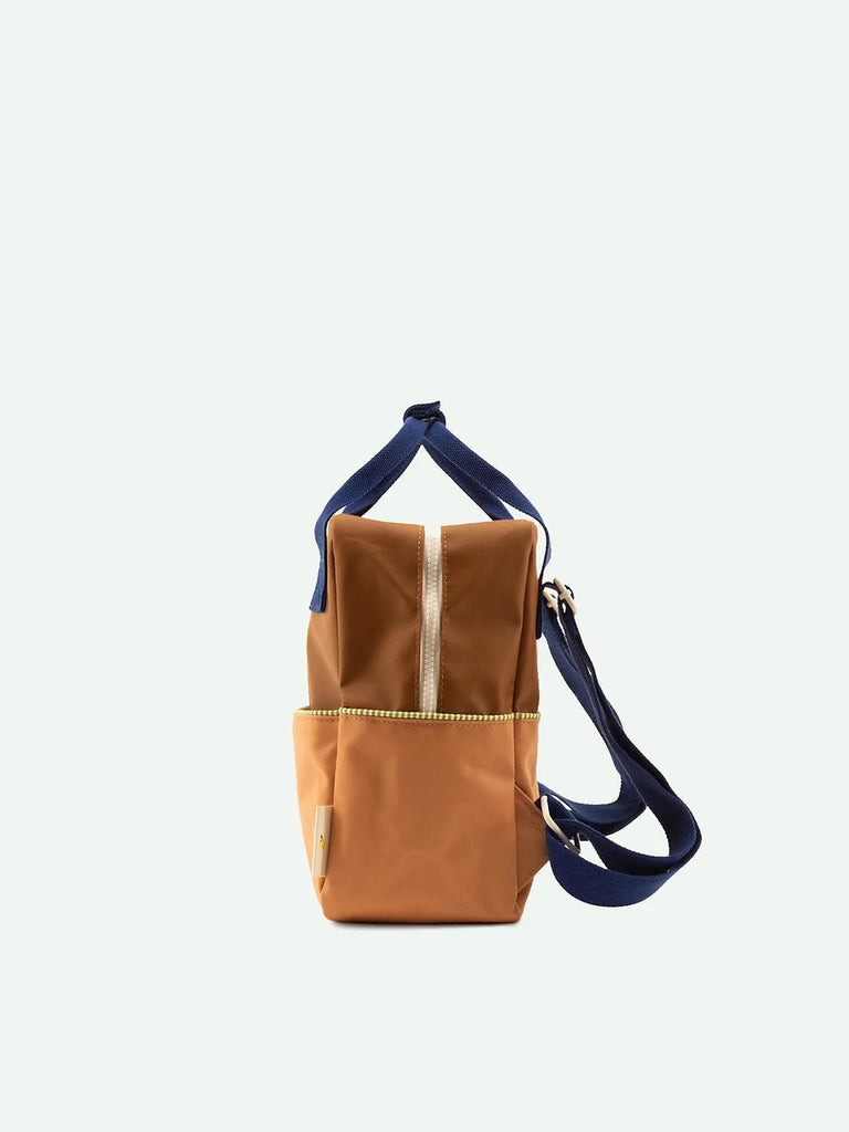 A Sticky Lemon Backpack Small in the Meet Me In The Meadows colorway, featuring a dark blue upper and Treehouse Brown lower section, with a convenient front pocket and a YKK zipper closure, displayed against a plain white background.