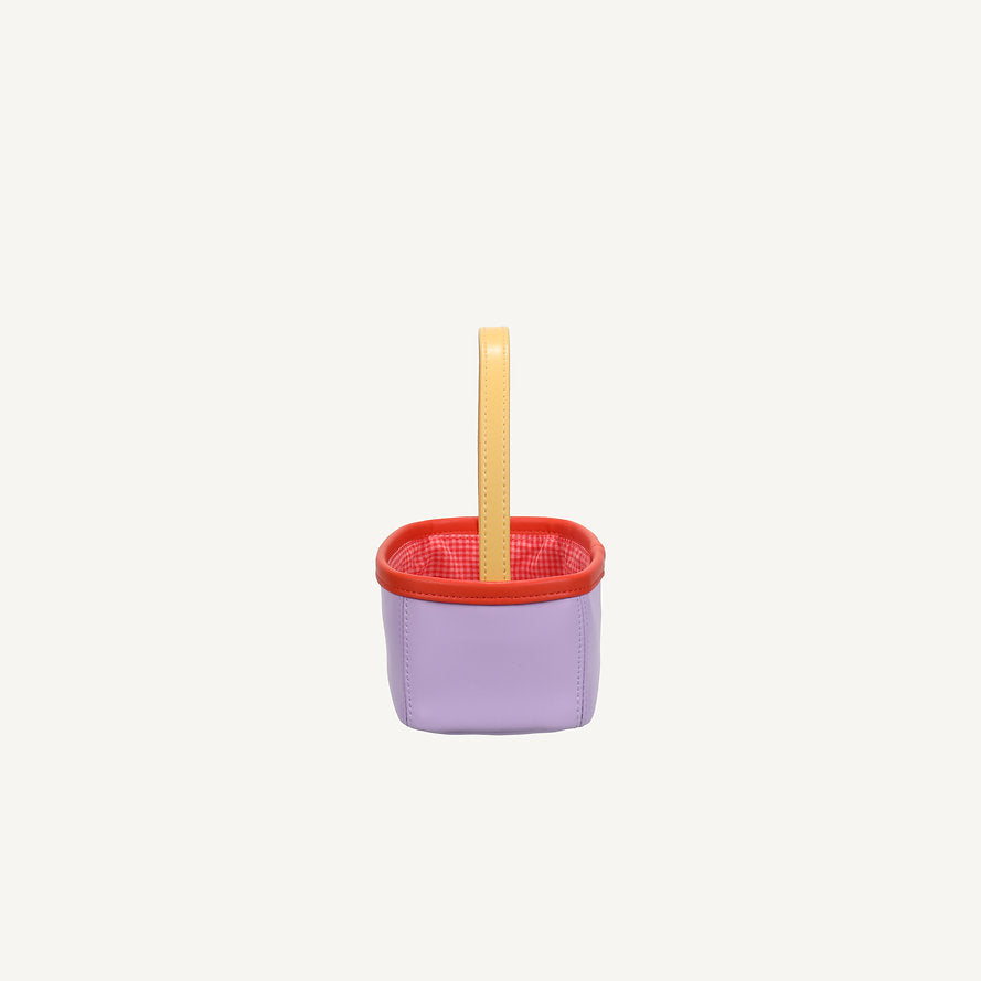 The Sticky Lemon Treasure Bag - Dewy Lilac features a small square shape with a purple body, red rim, yellow handle, and a red grid-patterned interior, displayed against a plain white background.