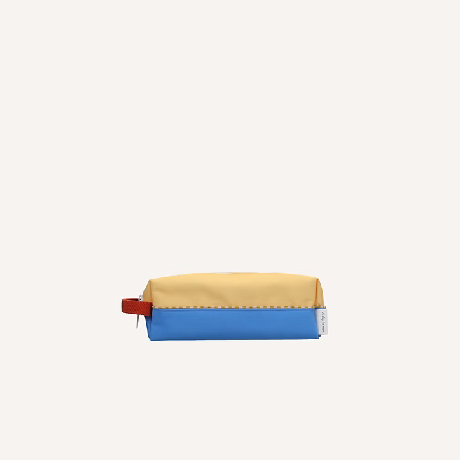 The Sticky Lemon Pencil Case | Color Blocking features a sandy yellow top, radar blue bottom, red side handle, white right-side tag, and YKK zipper—all made from recycled PET—shown on a plain light background.
