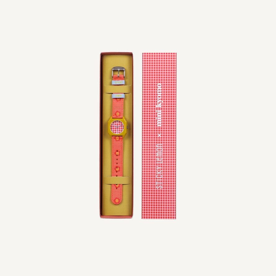 A playful Sticky Lemon x Mini Kyomo Watch - Flower in red and yellow with a checkered face sits in an open box, its matching red checkered lid with white text beside it—a vibrant addition to the Mini Kyomo watches collection.