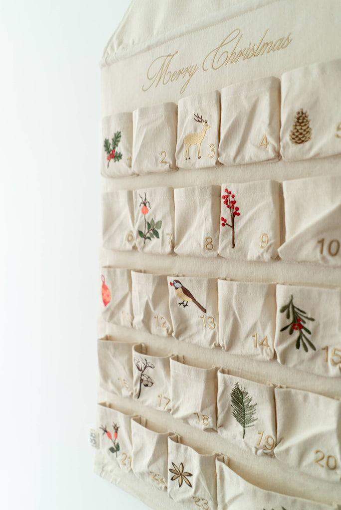 The Sabo Concept Christmas Cotton Advent Calendar hangs on the wall, featuring festive embroidery, "Merry Christmas" at the top, and 24 numbered pockets for a holiday countdown.