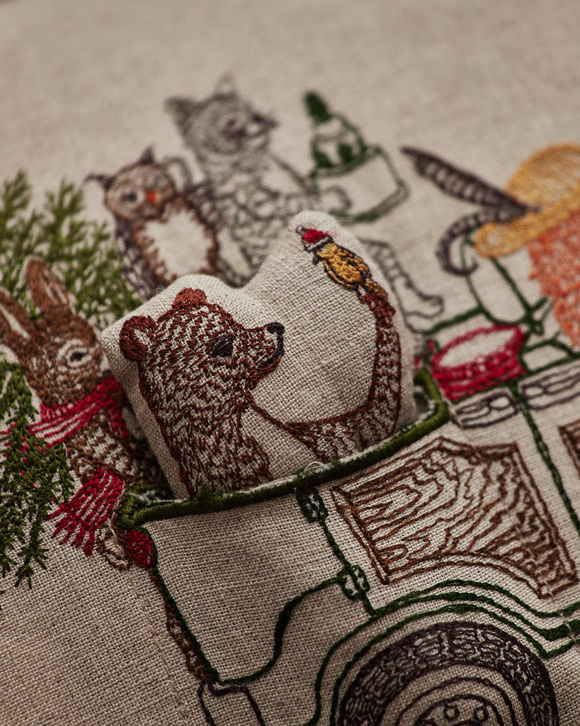 The Coral & Tusk Christmas Tree Car Pocket Pillow features embroidered woodland animals—a 3D bear, rabbit, fox, and cat—riding in a vintage car with a Christmas tree. The bear is three-dimensional and sits in the driver’s seat.