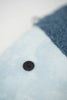 A single black button rests on a soft, light blue fabric with a Dark Blue Fish Pack towel, made in Spain, partially visible in the background.