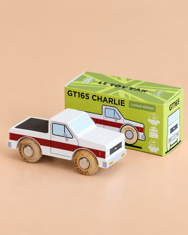 A wooden pick-up truck with red stripes sits beside a green and yellow box labeled “No. 30 GT165 Charlie | Made in England.” Perfect for fans of adventure toys, the truck features wooden wheels and a simple painted design, capturing the spirit of classic off-road vehicles.