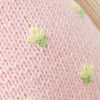Close-up of Cuddle + Kind Eleanor the Lamb’s pink knitted fabric, handmade in Peru, featuring small yellow and green embroidered flower designs scattered across the surface.