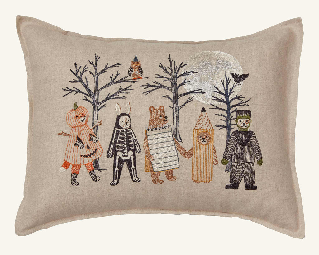 The Coral & Tusk Full Moon Masquerade Pillow features embroidered animals and a child in costume—pumpkin, skeleton, bear, notepad, pencil, Frankenstein—with bare trees, silver moon, owl, and bat for festive Halloween decor.